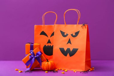 Alışveriş torbaları, hediye kutuları ve mor arka planda Cadılar Bayramı için lezzetli mısır şekerleri olan kompozisyon