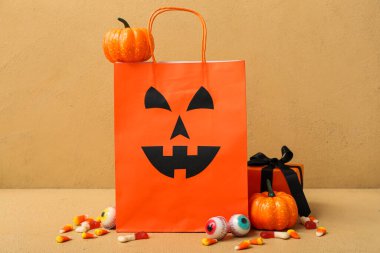 Bej arka planda Cadılar Bayramı için alışveriş torbası, balkabağı, hediye kutusu ve lezzetli şekerlerle kompozisyon