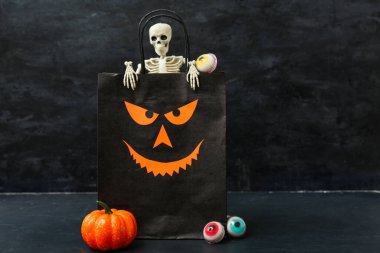 Alışveriş torbası, iskelet, balkabağı ve Cadılar Bayramı için tatlı şekerler içeren kompozisyon