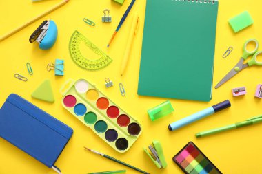 Sarı zemin üzerine farklı okul kırtasiyesi ve not defterleri.