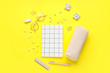 Sarı zemin üzerinde farklı kırtasiye malzemeleri ve gözlüklerle kompozisyon