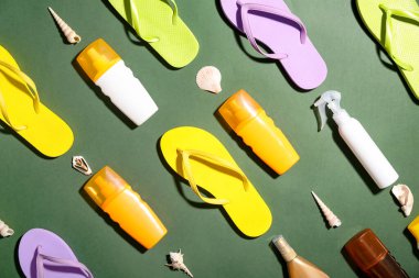 Farklı parmak arası terlikleri, güneş kremi ve yeşil arka planda deniz kabukları olan kompozisyon