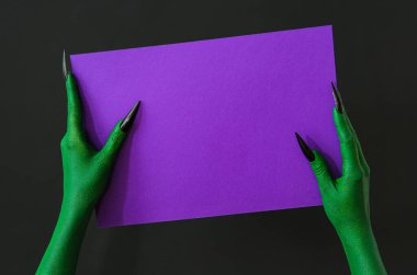 Siyah arka planda boş mor kağıt çarşaflı bir cadının elleri. Cadılar Bayramı