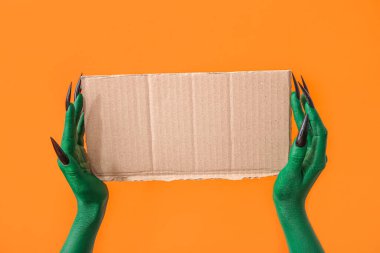 Turuncu arka planda boş kağıt çarşaf ile cadının yeşil elleri. Cadılar Bayramı