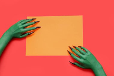 Kırmızı zemin üzerinde boş turuncu kağıt çarşaf olan cadının elleri. Cadılar Bayramı