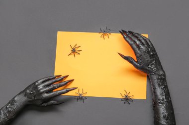 Boş turuncu kağıt çarşaflı ve gri arka planda örümcekleri olan bir cadının kara elleri. Cadılar Bayramı