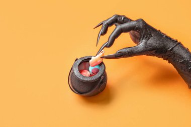 Cadıların kara eli kazan ve turuncu arka planda lezzetli şekerler, yakın plan. Cadılar Bayramı