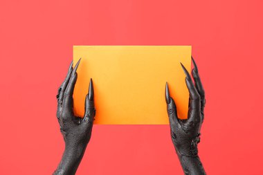 Kırmızı zemin üzerinde boş turuncu kağıt çarşaf olan bir cadının kara elleri. Cadılar Bayramı