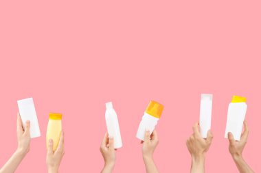 Pembe arka planda güneş kremi şişeleri olan kadın elleri.