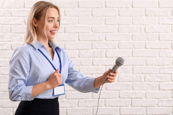 Журналистка с микрофоном на белом кирпичном фоне