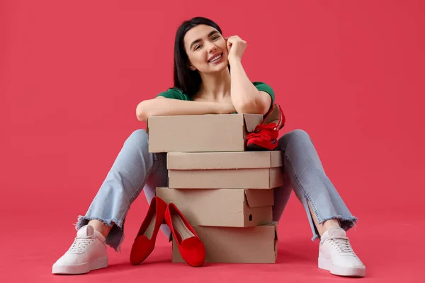 Young woman with shoe boxes sitting on red background