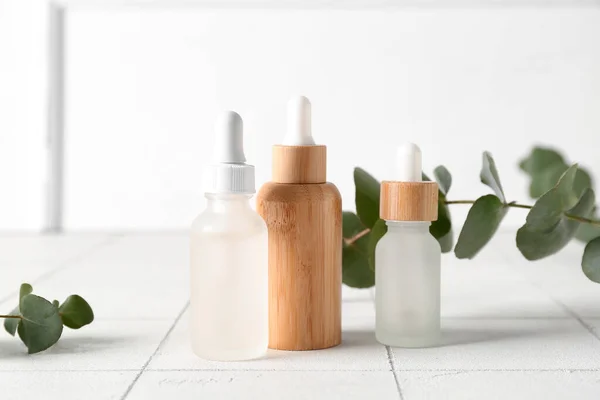 stock image Bottles of cosmetic oil and eucalyptus branches on white tile