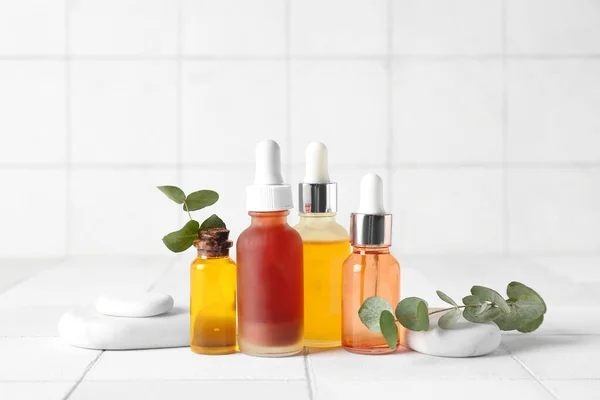 Zusammensetzung Mit Flaschen Kosmetiköl Wellnesssteinen Und Eukalyptuszweigen Auf Weißen Fliesen — Stockfoto