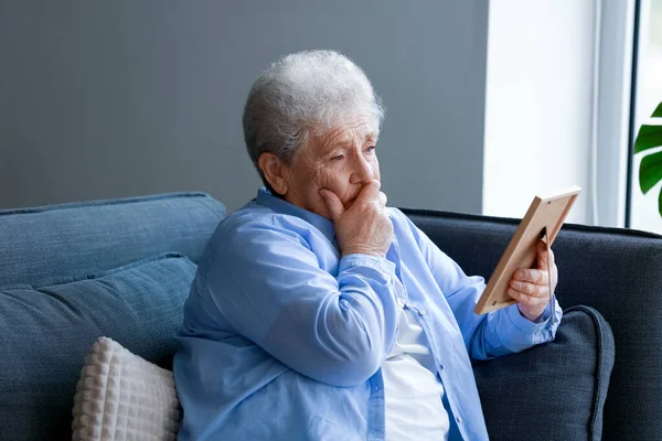闷闷不乐的老妇人 她的相框坐在家里的沙发上 — 图库照片