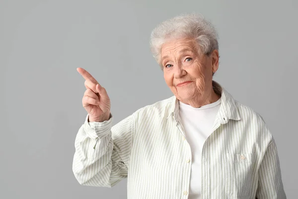 Senior Vrouw Wijzend Naar Iets Grijze Achtergrond — Stockfoto