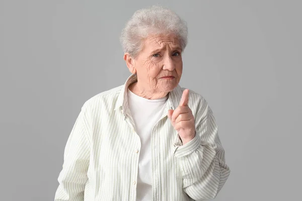 Gri Arka Planda Işaret Parmağı Kaldırılmış Yaşlı Bir Kadın — Stok fotoğraf