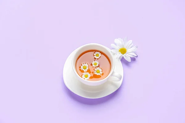 stock image Cup of natural chamomile tea with flower on lilac background