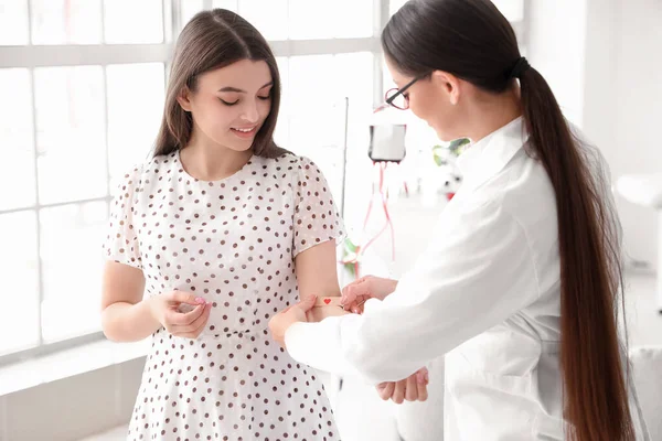 Female doctor applying medical patch on young donor's arm in clinic