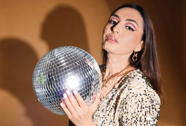 stock image Fashionable beautiful woman in sparkling dress with disco ball on orange background