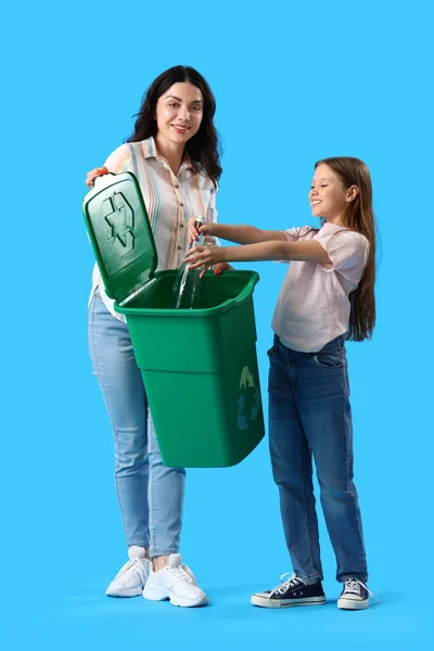 彼女の母親と小さな女の子は 青い背景にリサイクルビンにガラス瓶を投げる — ストック写真