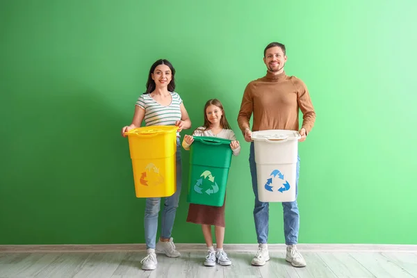 Family with recycle bins near green wall