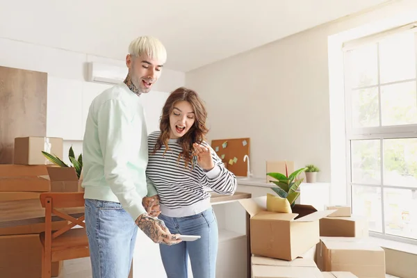 Young couple with keys from their new flat taking selfie in kitchen on moving day