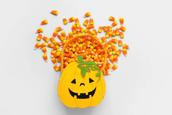 Bag in shape of pumpkin with tasty Halloween candy corns on light background