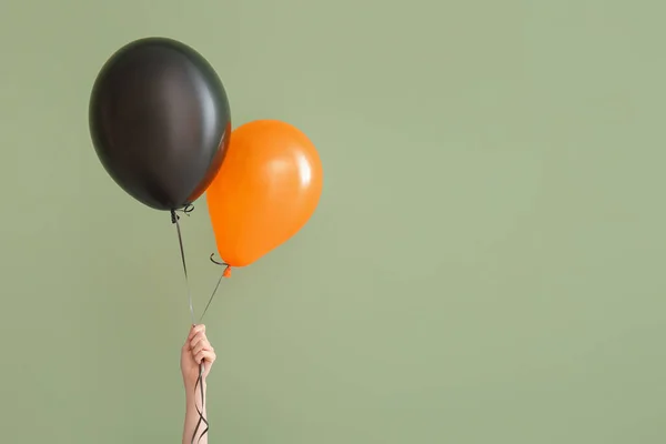 Female hand with different Halloween balloons on green background