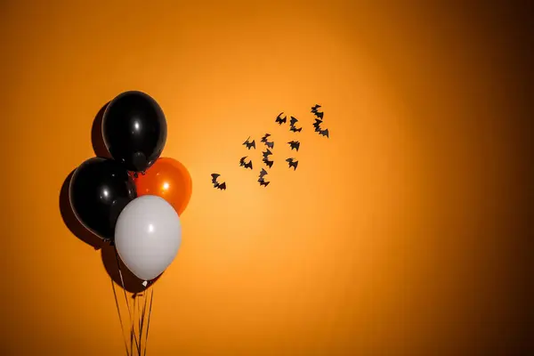 Halloween balloons and bats hanging on orange wall in room