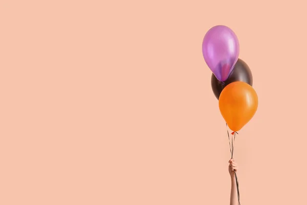 Female hand with different Halloween balloons on beige background