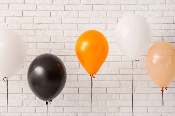 Different Halloween balloons near light brick wall in room
