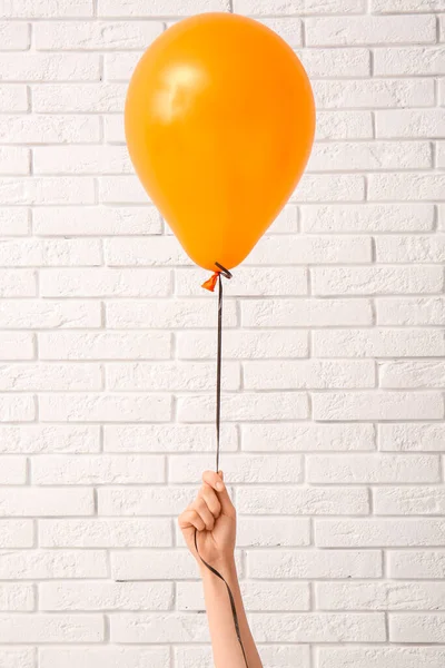 Female hand with orange Halloween balloon near light brick wall in room