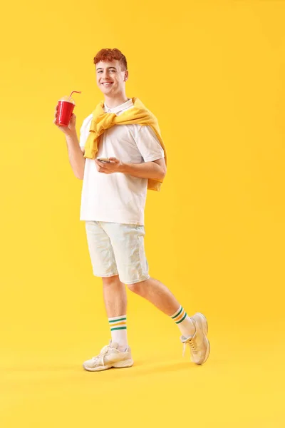 Junger Rothaariger Mann Mit Tasse Limo Und Handy Auf Gelbem — Stockfoto