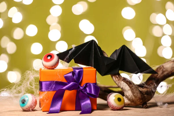 Composition with beautiful gift box, wood and tasty candies for Halloween on table against blurred lights, closeup