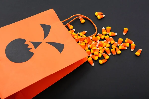 Composition with shopping bag and tasty candy corns for Halloween on dark background, closeup