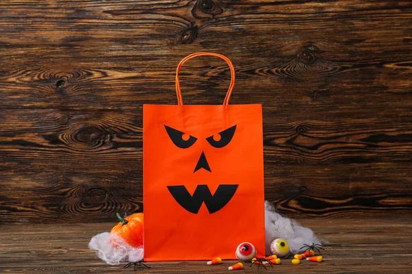 Composition with shopping bag and tasty candies for Halloween on wooden background