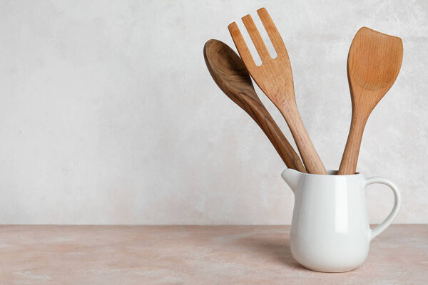 Pitcher with wooden cutlery on light background