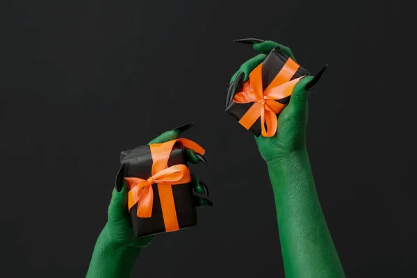 Green hands of witch with gift boxes on dark background. Halloween celebration