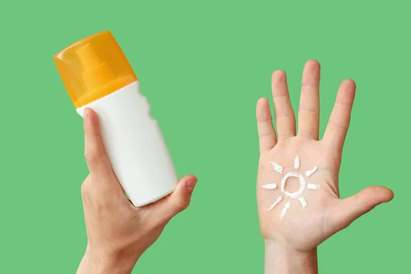 Female hand with sun made of sunscreen cream on green background