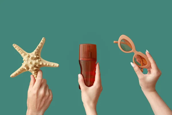 Female hands with bottle of sunscreen cream, sunglasses and starfish on green background