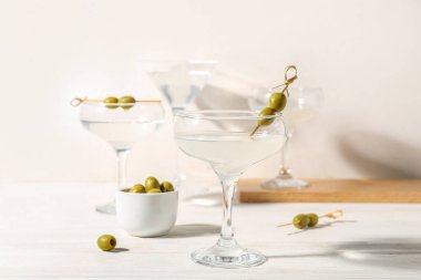 Beyaz ahşap masada zeytinli bir bardak martini.