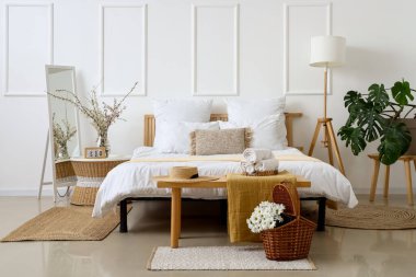 Hafif yatak odasının içinde, sepetinde kasımpatı çiçekleri ve komodinin üzerinde çiçek açan ağaç dalları olan.