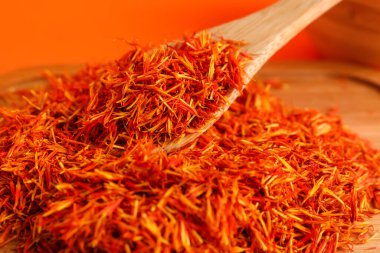 Ahşap tahta ve kaşık, turuncu arka planda safran yığını.