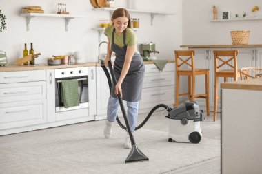 Mutfakta halı süpüren genç bir kadın.