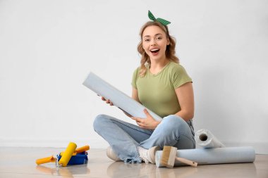 Duvar kağıdı rulosu olan genç bir kadın evde oturuyor.