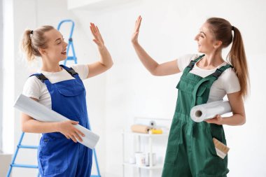 Duvar kâğıdı ruloları olan kadın dekoratörler odada birbirlerine beşlik çakıyorlar.