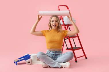 Pembe arka planda duvar kağıtları yuvarlanan mutlu genç bir kadın.