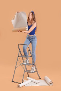 Duvarda yuvarlanan duvar kağıtlarıyla bej arka planda genç bir kadın.