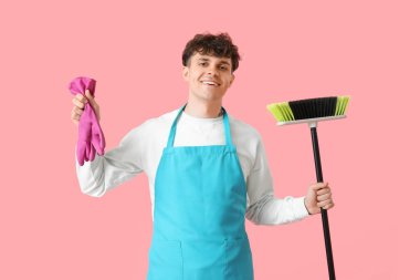 Pembe arka planda süpürge ve lastik eldivenli erkek hademe.