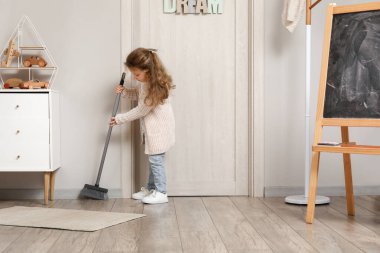 Evinde süpürgeyle yerleri süpüren sevimli küçük kız.